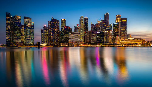 Illuminated buildings by river against sky