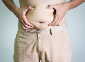 Midsection of man holding belly against gray background