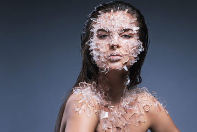 Portrait of woman with broken glass on body against purple background