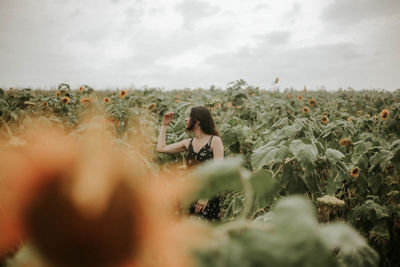 Young woman standing amidst sunflowers on field