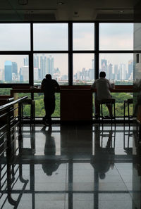 Man and woman standing by railing against window in city