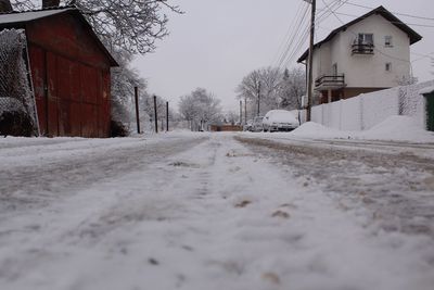 Snow covered road by houses against sky