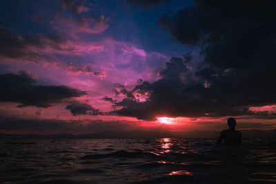 Silhouette woman in sea against sky at sunset