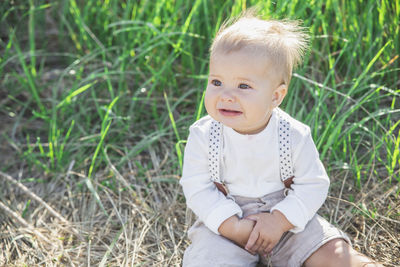 Beautiful blond baby in a suit with suspenders sits in the grass