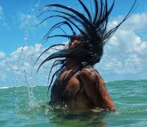 Side view of man splashing hair in sea against cloudy sky