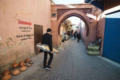 Rear view of man carrying skateboards while walking on footpath