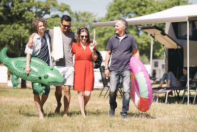 Happy family with inflatable rings walking on grassy field by travel trailers