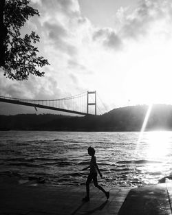 Silhouette person walking on promenade by river against cloudy sky during sunset