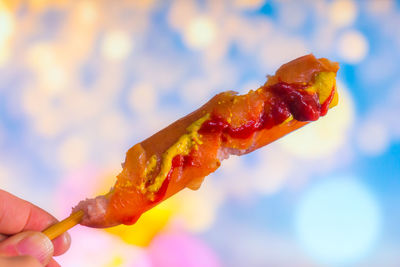 Cropped hand holding sausage covered with sauces