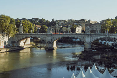 Arch bridge over river in city against clear sky