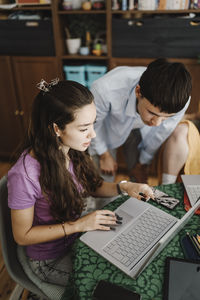 High angle view of male and female siblings discussing over laptop while studying at home