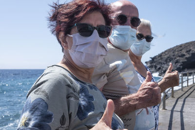 Portrait of smiling senior people gesturing against sea and sky