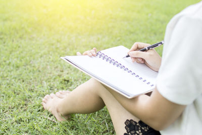 Low section of woman writing in book on field