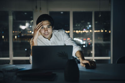 Businessman looking at laptop while working late in dark creative workplace