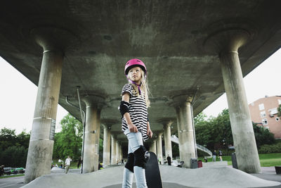 Low angle view of confident girl with skateboard standing at park