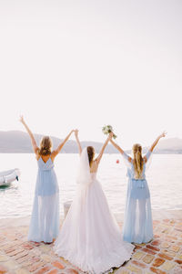 Rear view of bride with bridesmaid standing at beach against clear sky