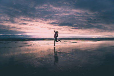 Woman jumping at beach against sky during sunset