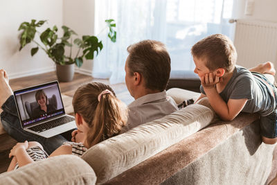 Video call using laptop from home. dad and children sit on the couch and call mom 
