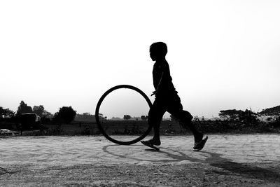 Silhouette boy playing with tire on land against clear sky