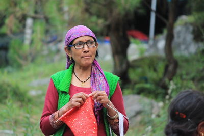 Woman knitting wool while looking away against trees