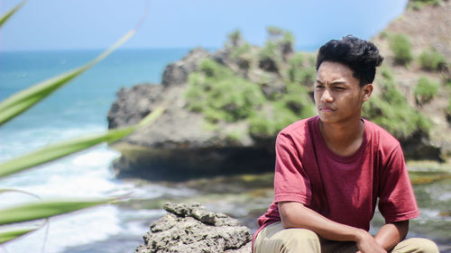 Young man sitting on rock by sea