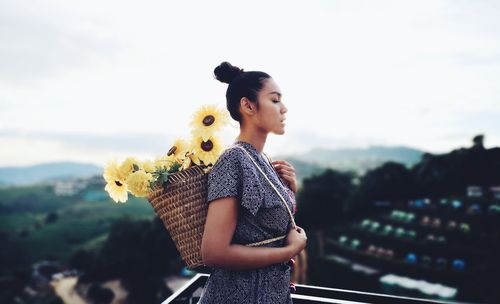 Woman carrying flowers in basket while standing at terrace