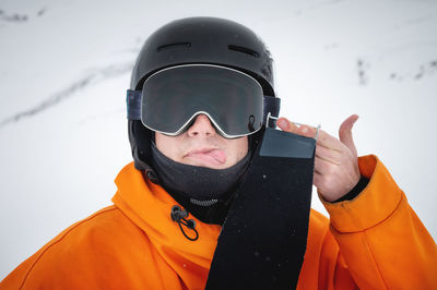 A young skier stands on a mountain slope in winter, showing his tongue