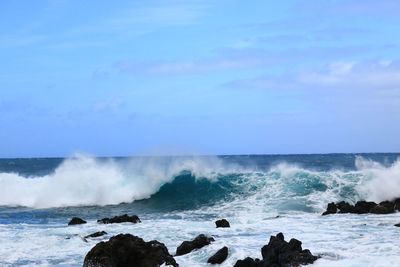 Waves splashing on rocks against sky