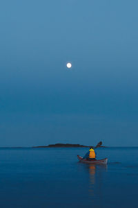 A kayaker paddles towards the moon.