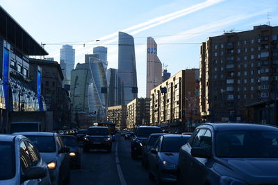 Cars on road by buildings against sky in city