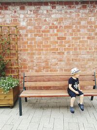 Coy sitting on bench against brick wall