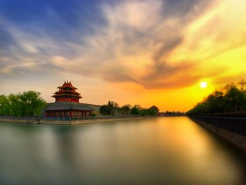 Traditional building by moat at forbidden city during sunset