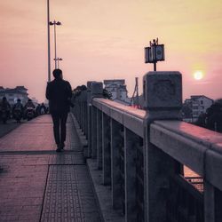 Rear view of man walking on street against sky during sunset