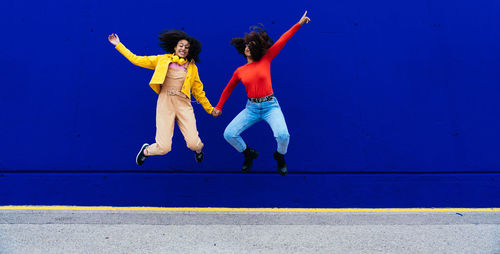 Cheerful friends jumping against blue wall