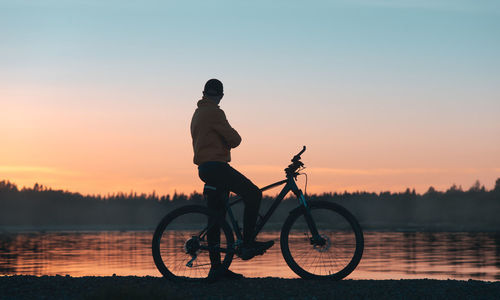 Silhouette man riding bicycle on lake against sky during sunset