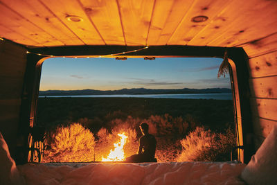 Rear view of man sitting by window at sunset