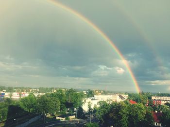 Rainbow over trees against cloudy sky