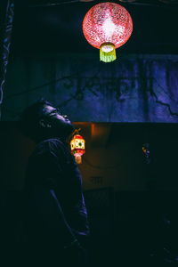 Rear view of woman standing by illuminated lantern at night