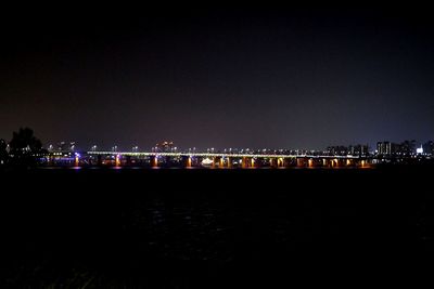 Illuminated buildings by sea against clear sky at night