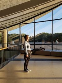 Woman standing by railing against window