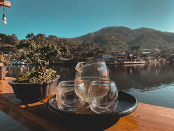 Drinking glass on table by lake against sky