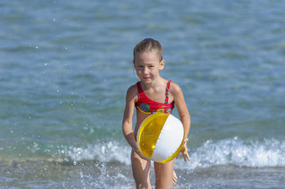 Portrait of smiling girl with ball running on beach