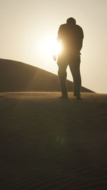 Rear view of silhouette man standing against sun during sunset