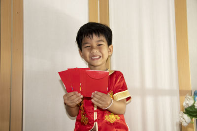 Happy boy holding red while standing against wall