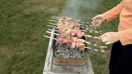 Midsection of person preparing meat on barbecue at lawn