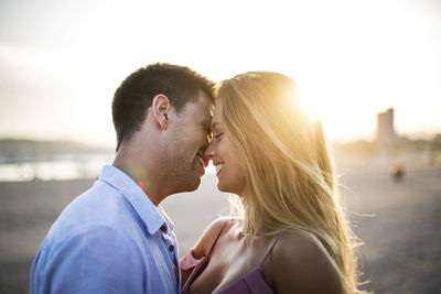 Smiling couple kissing while standing against sky during sunset