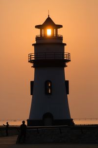 Silhouette building by lighthouse against sky during sunset