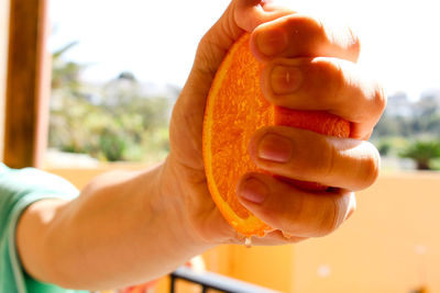 Close-up of cropped hand squeezing orange