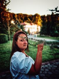 Portrait of young woman against plants during sunset