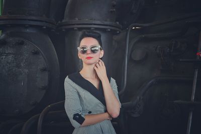 Young woman wearing sunglasses standing against machinery at factory